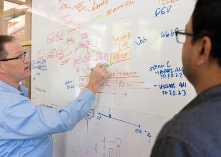 Two men work out a problem on a whiteboard.
